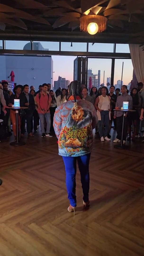 Lisa Francoeur seen from behind in a colorful jacket and blue trousers at an indoor event